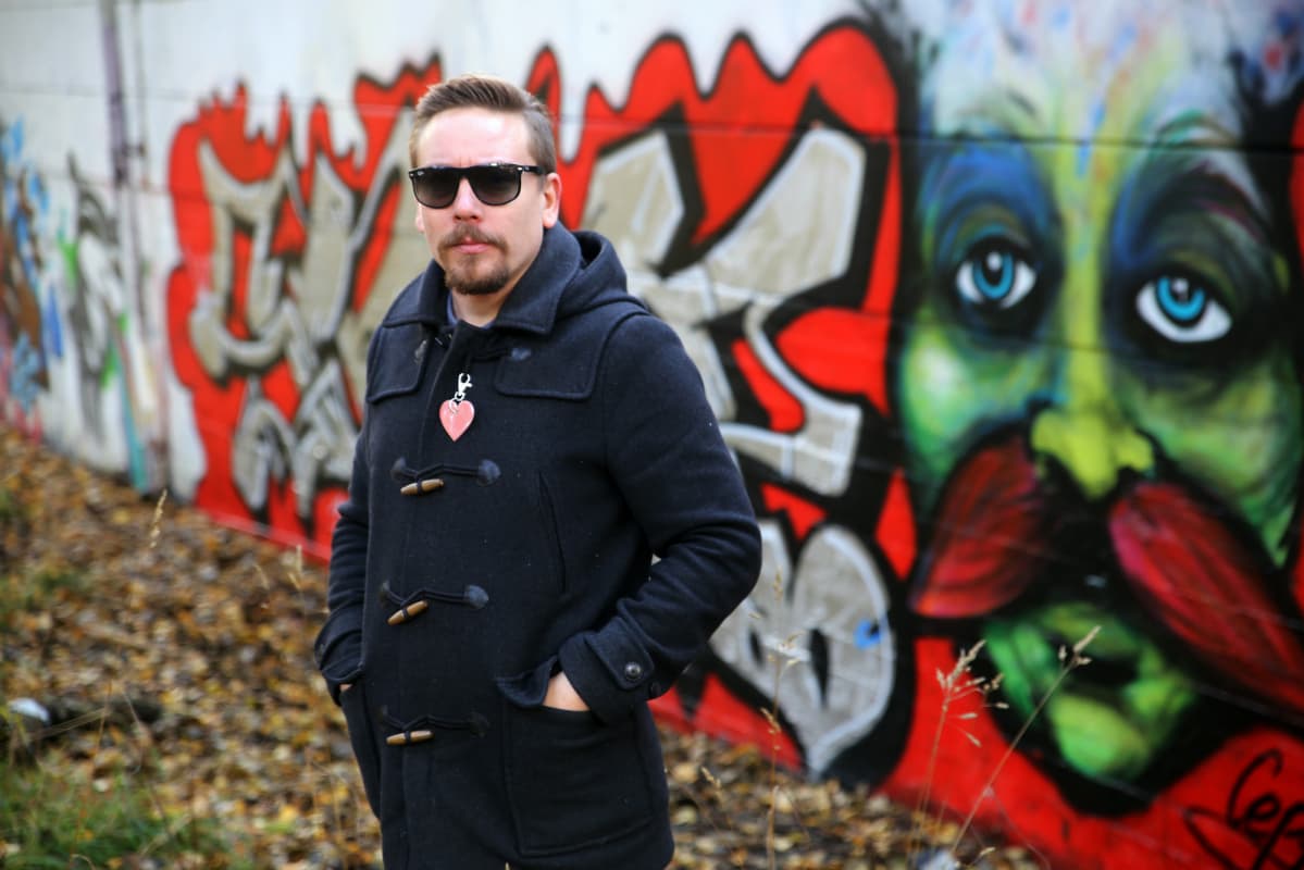 Mies seisoo aurinkolasit päässä graffitiseinän edessä