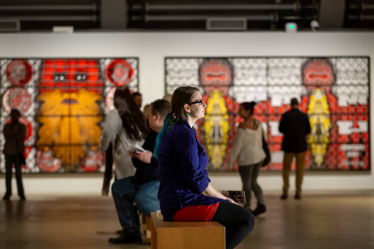 Mira Jaskari istuu ja katselee Gilbert & George -taiteilijaparin näyttelyä Helsingin taidemuseossa.