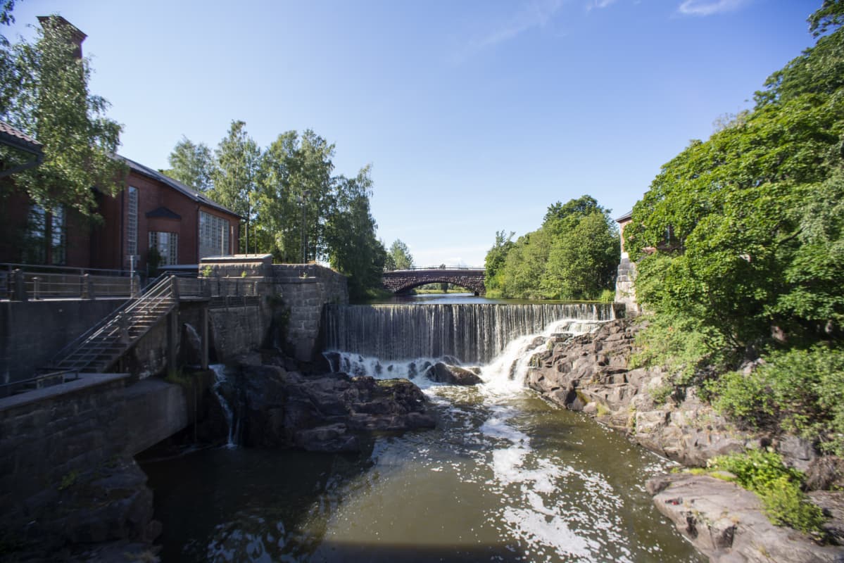 En fors, med en damm och ett vattenfall i mitten. Vattnet är grönbrunt. Det är en solig dag, himlen är blå.