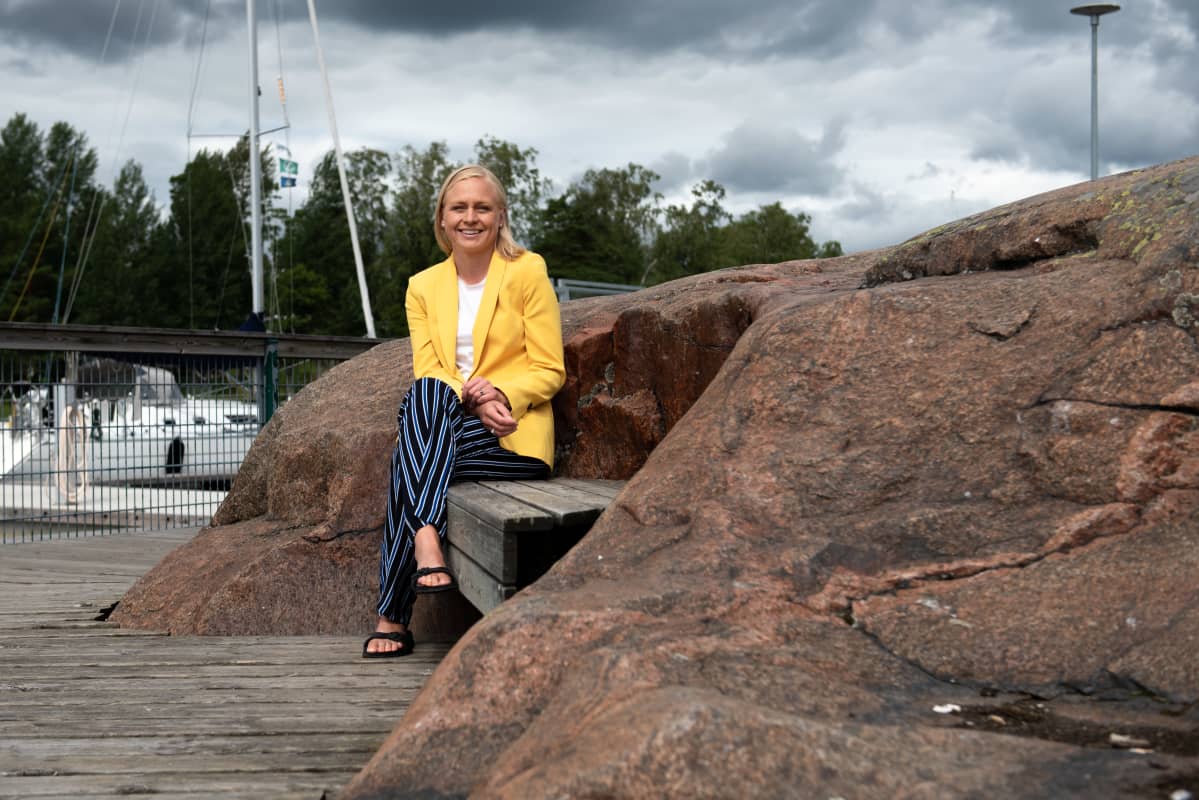 Elina Lepomäki istuu penkillä kallion kupeessa.