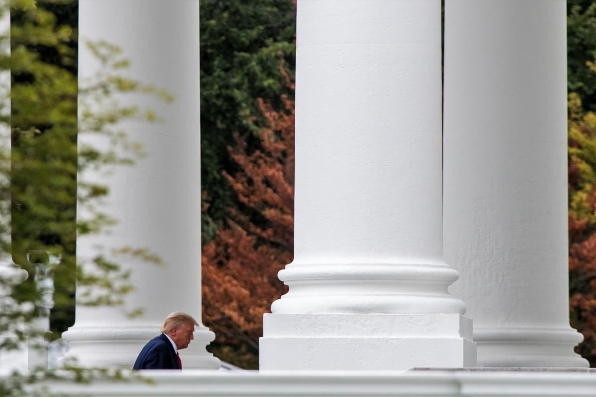 Trump kulkee suurten valkoisten pylväiden välistä. Taustalla näkyy aavistuksen syksyistä lehvästöä.