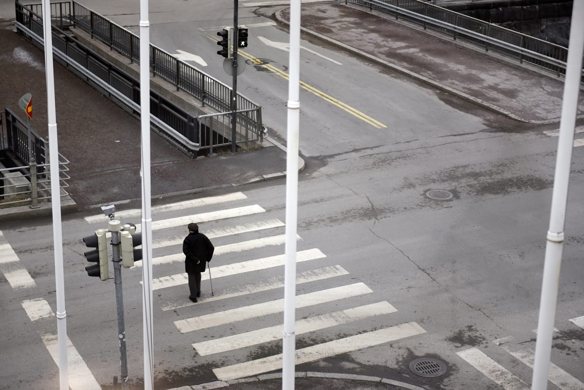 Yksinäinen vanhus kävelee suojatiellä.