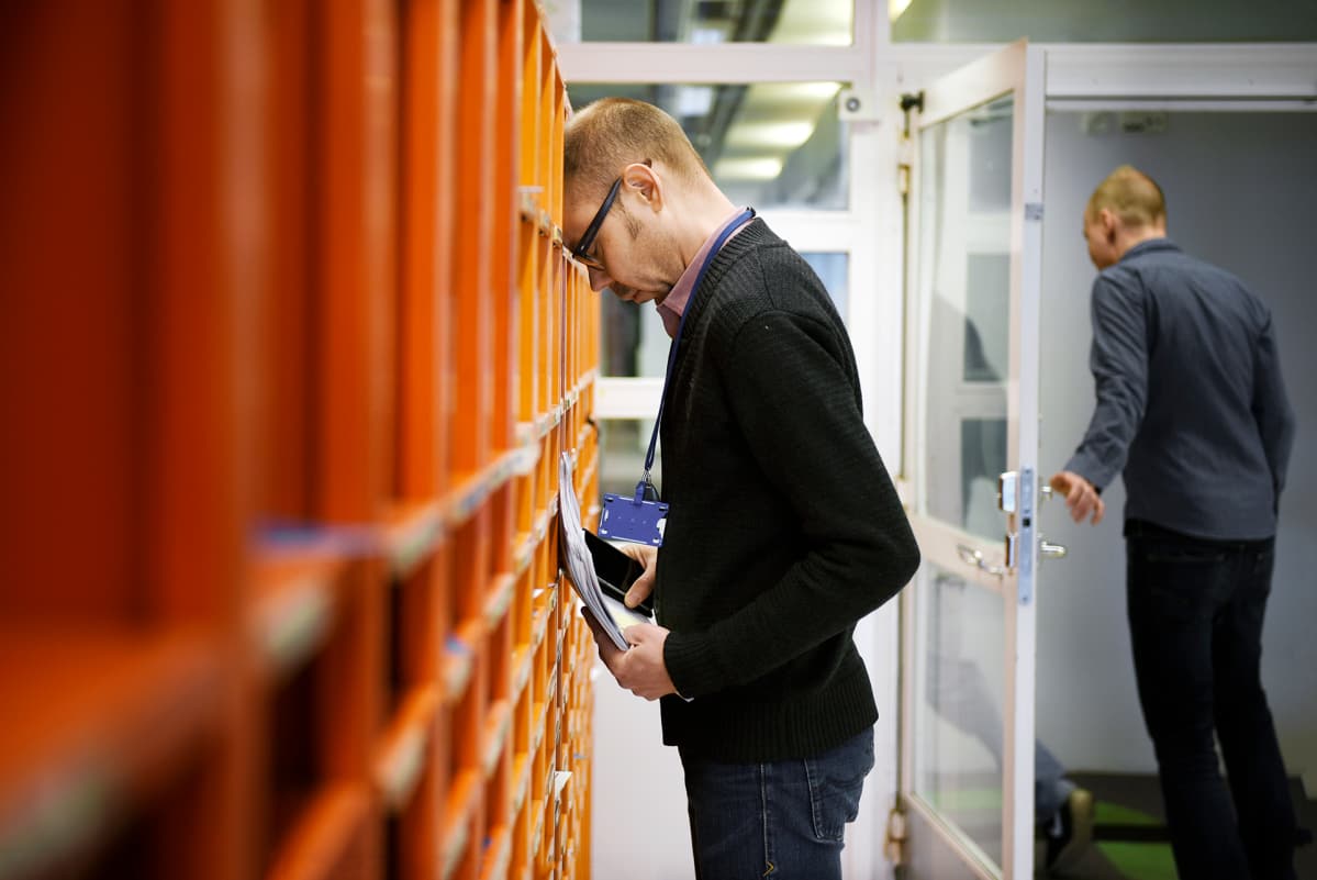 Työntekijä nojaa työpaikkansa postilokerikkoon.