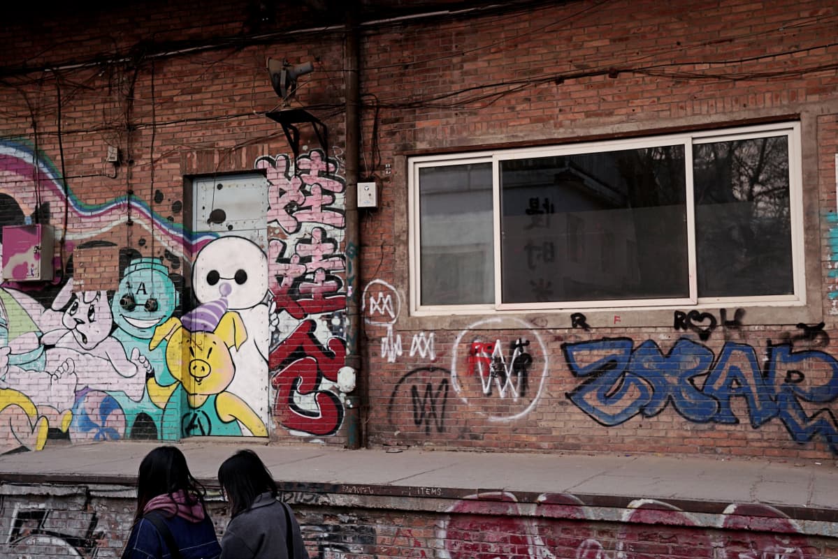 Graffitiseinä ja kaksi nuorta naista selin.