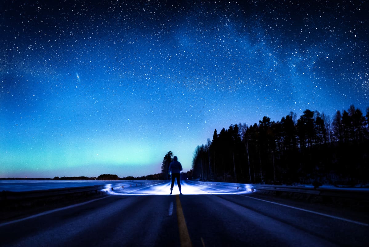 Ihminen seisoo tiellä tähtitaivaan alla.