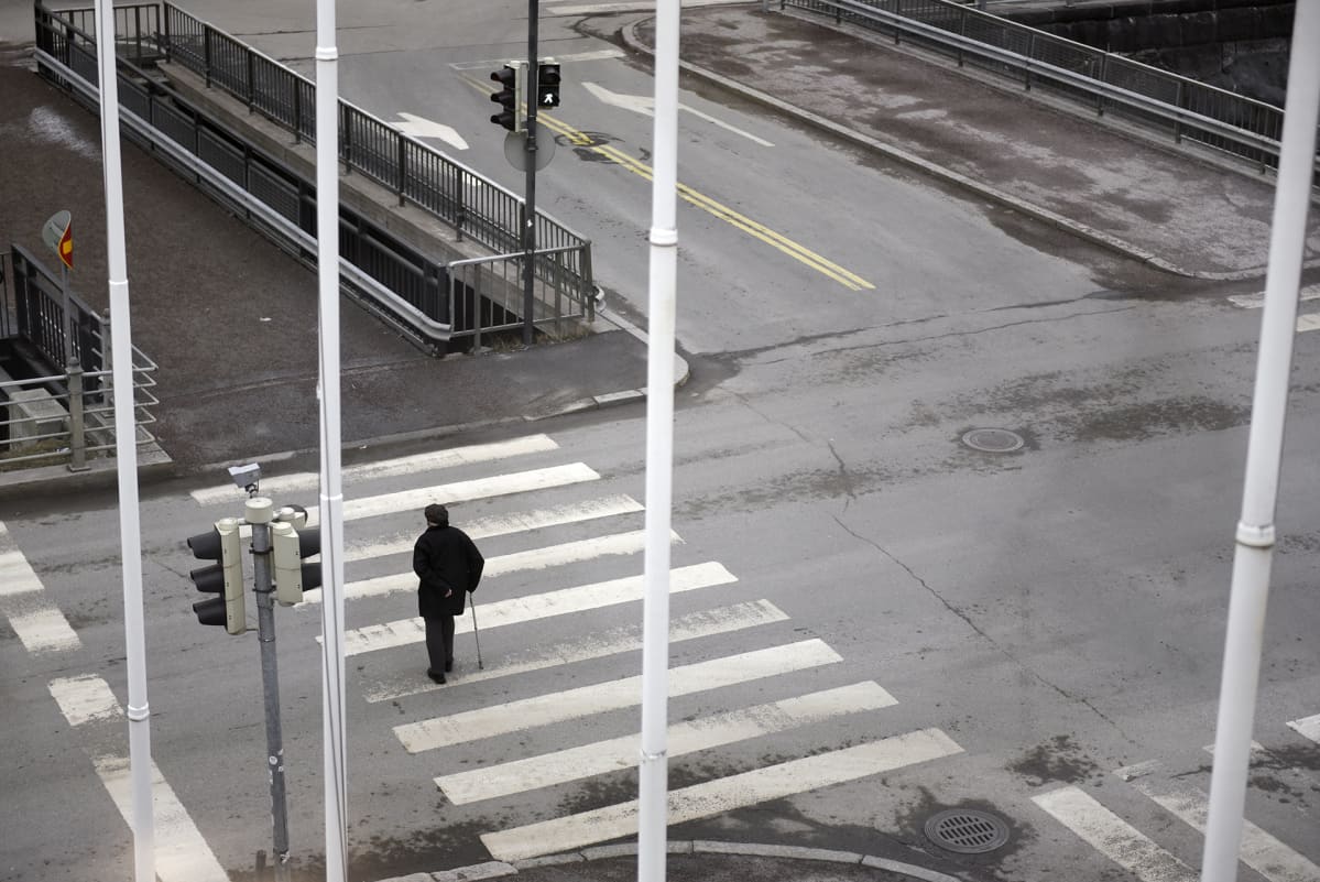 Yksinäinen vanhus kävelee suojatiellä.