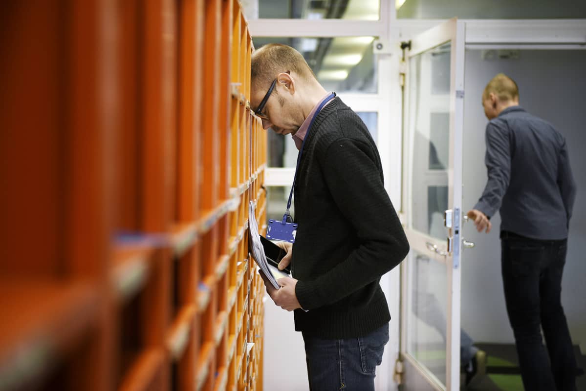 Työntekijä nojaa työpaikkansa postilokerikkoon.