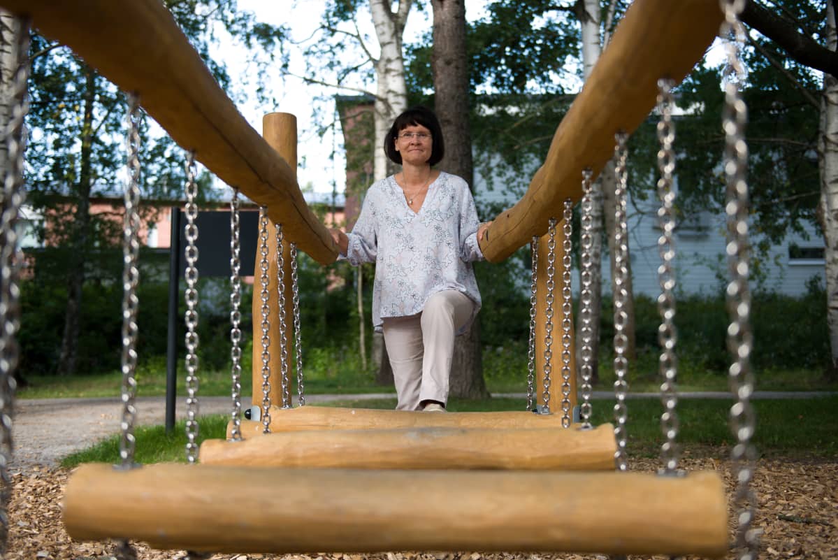 Sirpa Huttunen nousemassa riippusilta-leikkitelineeseen.