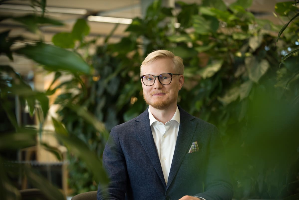 Visa Myllyntaus istumassa pöydän ääressä jonka ympärillä on paljon viherkasveja.