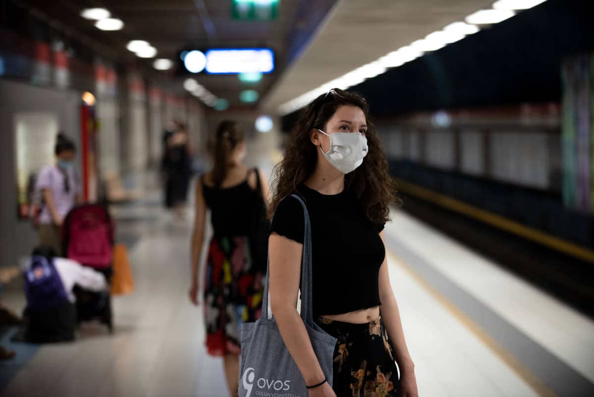 Nainen odottaa metroa maski päässään.