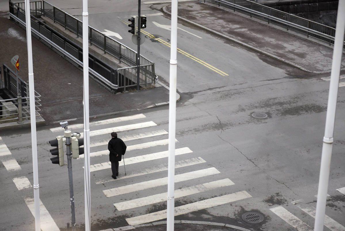 Yksinäinen vanhus kävelee suojatiellä.