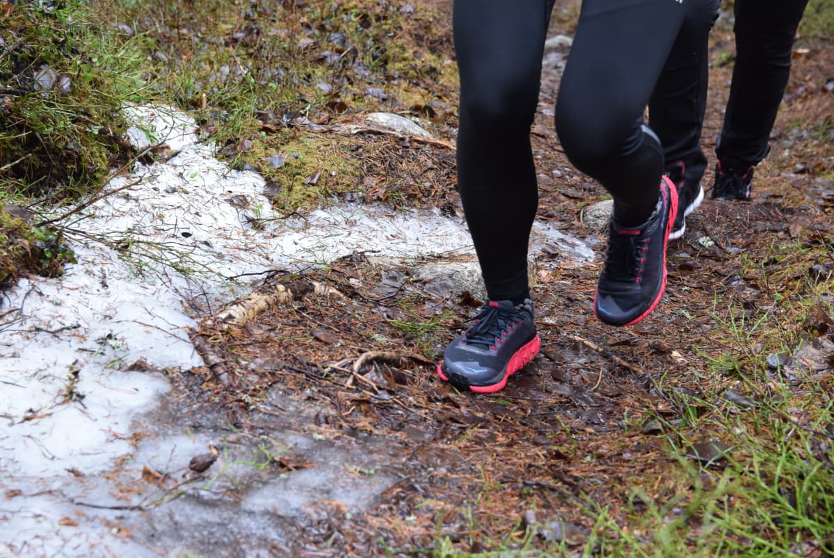 Närbild av fötter med gymnastikskor som pringer på en skogsstig med lite snö på.