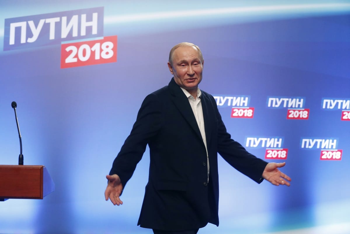 Vladimir Putin puku yllään, levittelee käsiään.