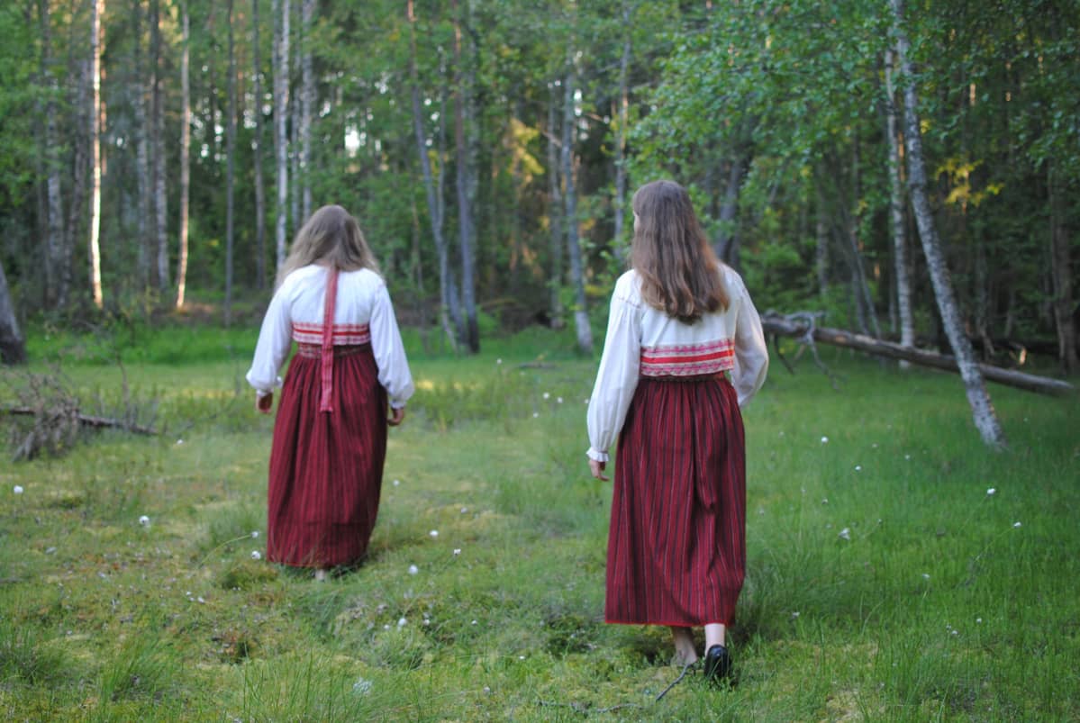 Lumi Rinne ja Säde Rinne kävelevät poispäin kamerasta Lavansaaren kansallispuvut yllään.