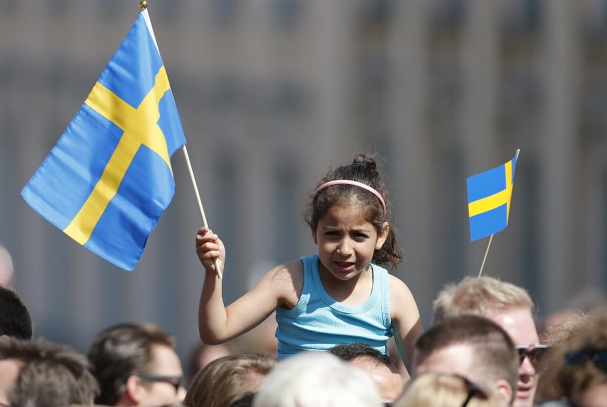 Pikkutyttö istuu aikuisen harteilla ja heiluttaa Ruotsin lippua.