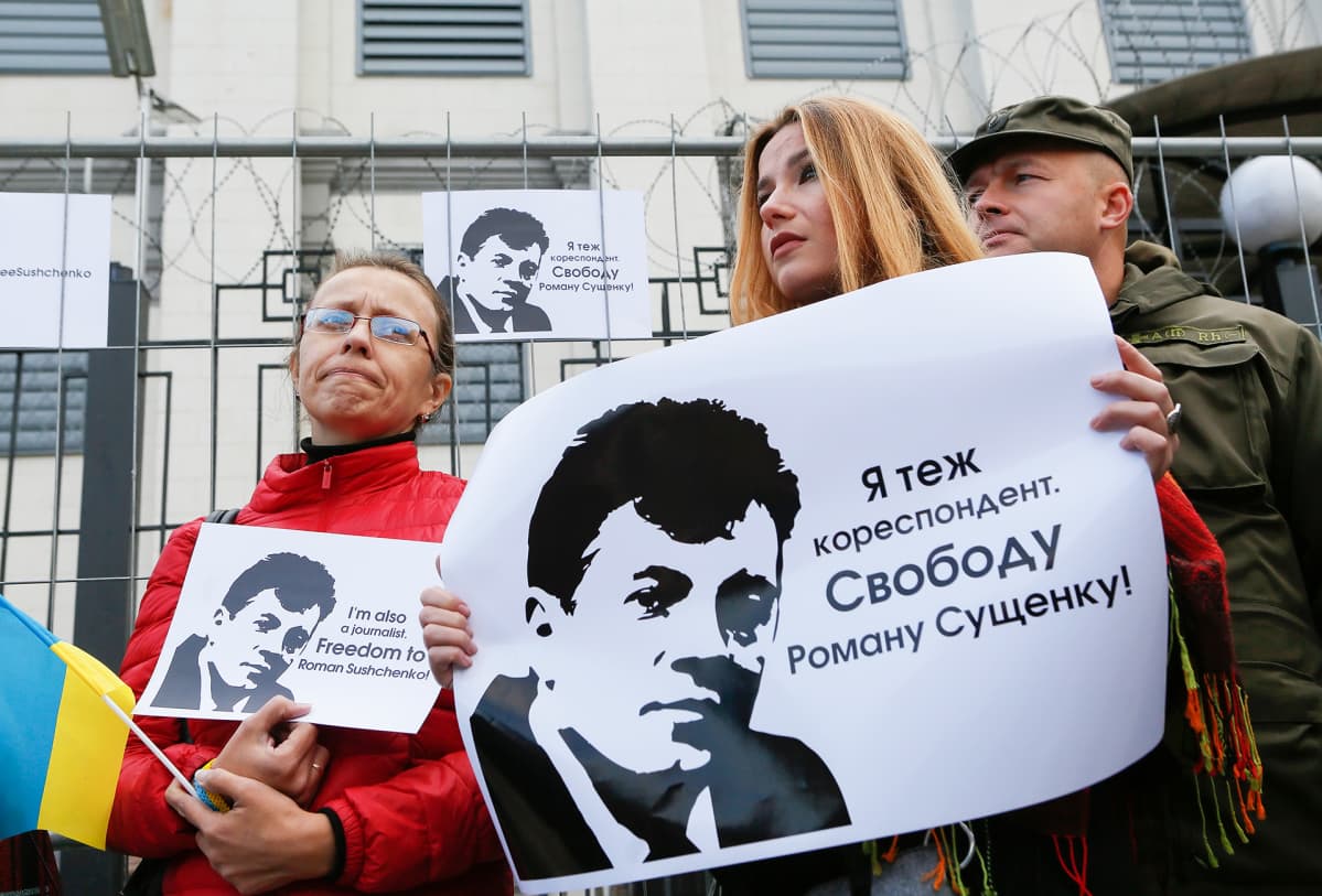 Ukrainalaisjournalistit pitelevät julisteita, joissa vaaditaan Roman Suštšenkon vapauttamista. Taustalla näkyy Venäjän suurlähetystö, jota suojelee piikkilangalla varustettu metalliaita.