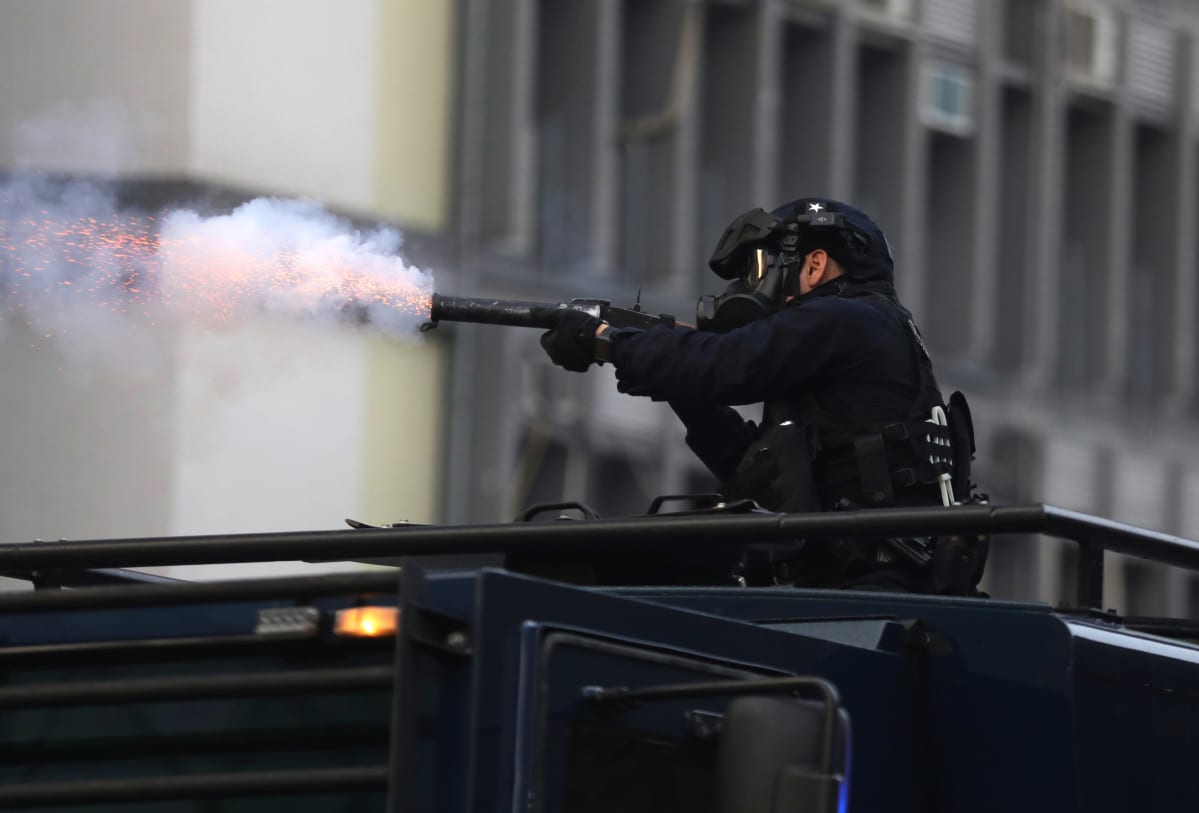 Mellakkavarusteinen poliisi ampuu kyynelkaasua.