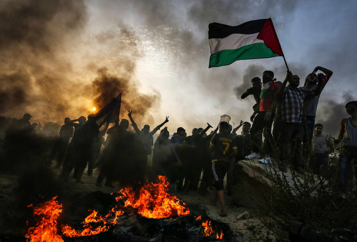 Palestiinalaisten lippu liehuu tulen ja mustan savun keskeltä Gazassa 22. lokakuuta.
