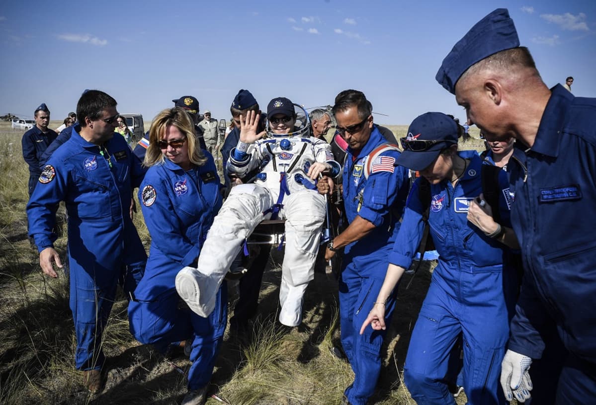 Nasan työntekijät kantavat vilkuttavan astronautin istuintia.