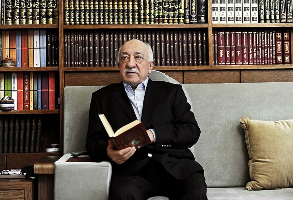 Fethullah Gülen istuu harmaalla sohvalla, iso kirjahylly takanaan.