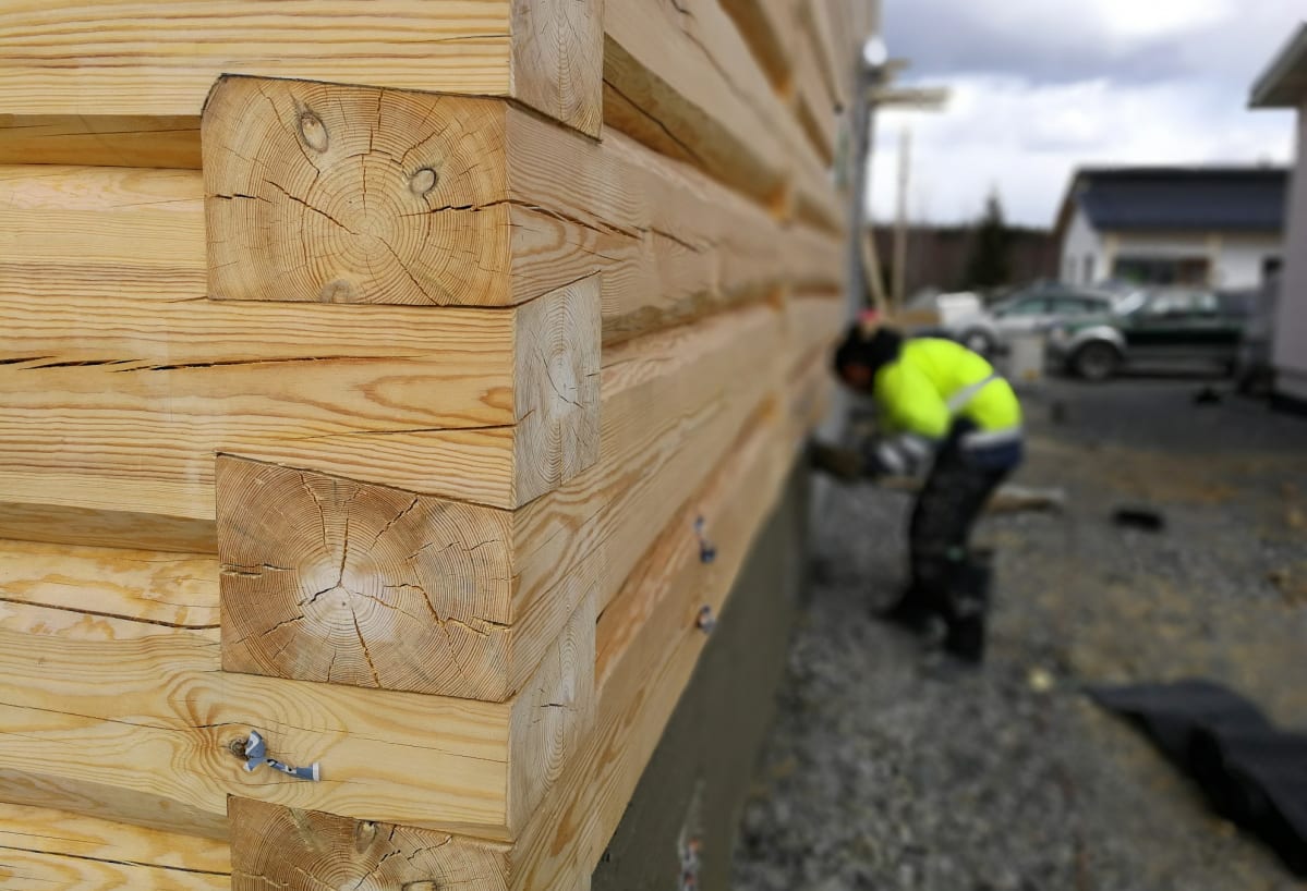 Hirsitalon ulkonurkka, taustalla mies rappaa kivijalkaa