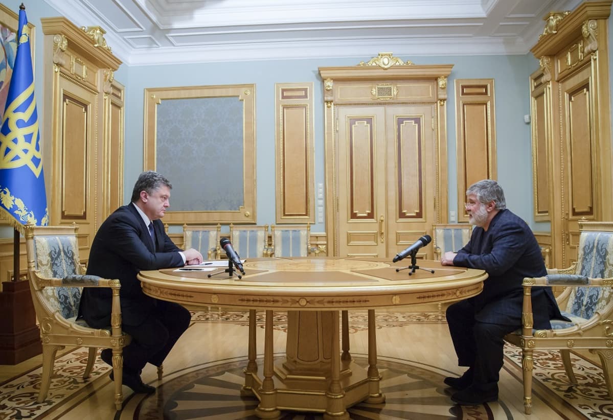 Petro Porošenko ja Ihor Kolomoiskyi istuvat salissa vastakkaisilla puolilla pöytää. Miesten edessä pöydällä on mikrofonit. Porošenkon takana on Ukrainan lippu.