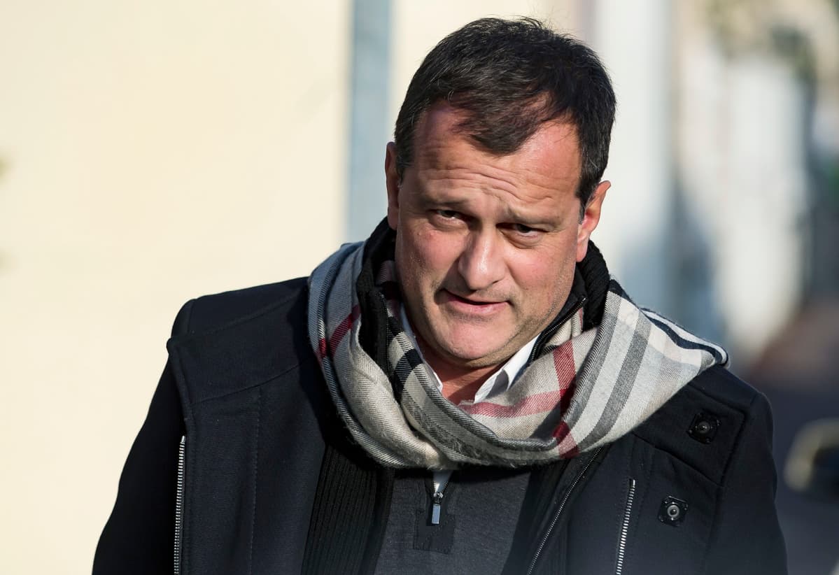 Louis Aliot kävelee mustassa päällystakissa, kaulaliina huolettomasti kietaistuna kohti kameraa.