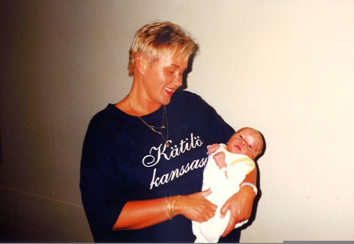Tarja Kovalainen pitelemässä lasta. Paidassa lukee kätilö kanssasi.