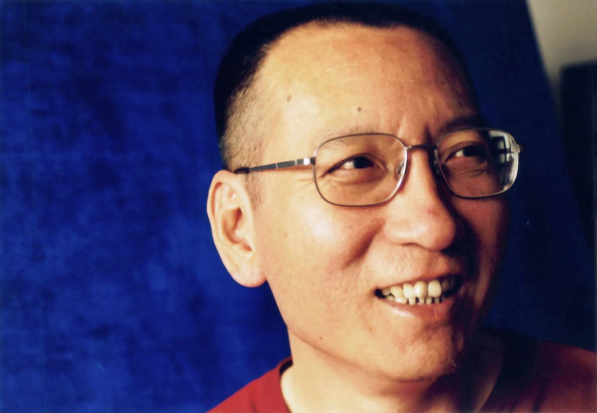 Liu Xiaobo hymyilee sinistä taustaa vasten.