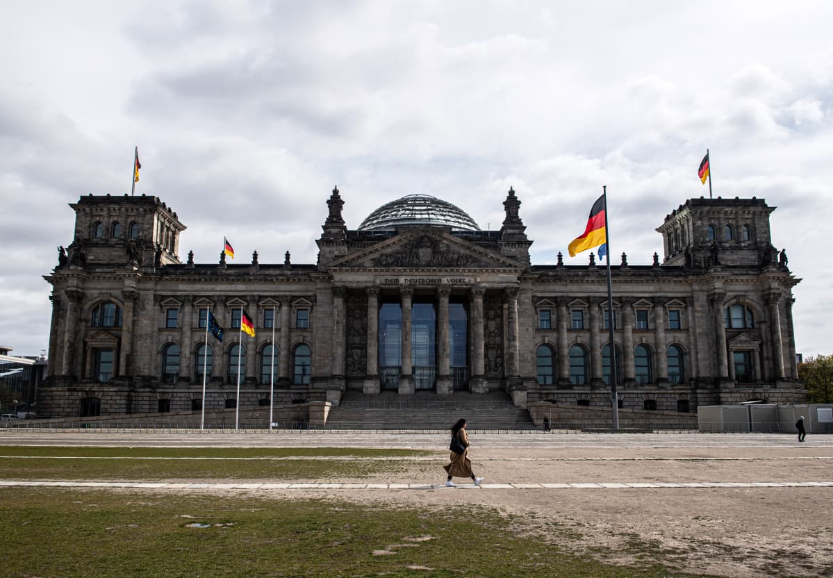 Nainen kävelee parlamenttirakennus Reichstagin edustalla koronan hiljentämässä Berliinissä. Suositut turistikohteet ovat nyt autioita.