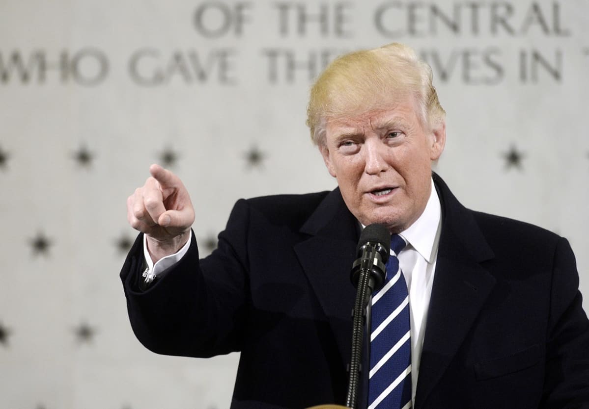 Trump puhuu osoittaen kuulijoita oikean kätensä etusormella. Taustalla näkyy CIA:n päämajan seinää, jossa muistetaan tähdillä palveluksessa kuolleita CIA:n työntekijöitä.