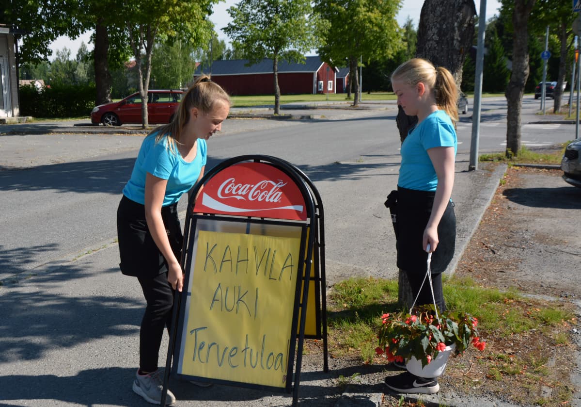 Vilma Kivelä ja Venni Valli viemässä kylttiä tien varteen.
