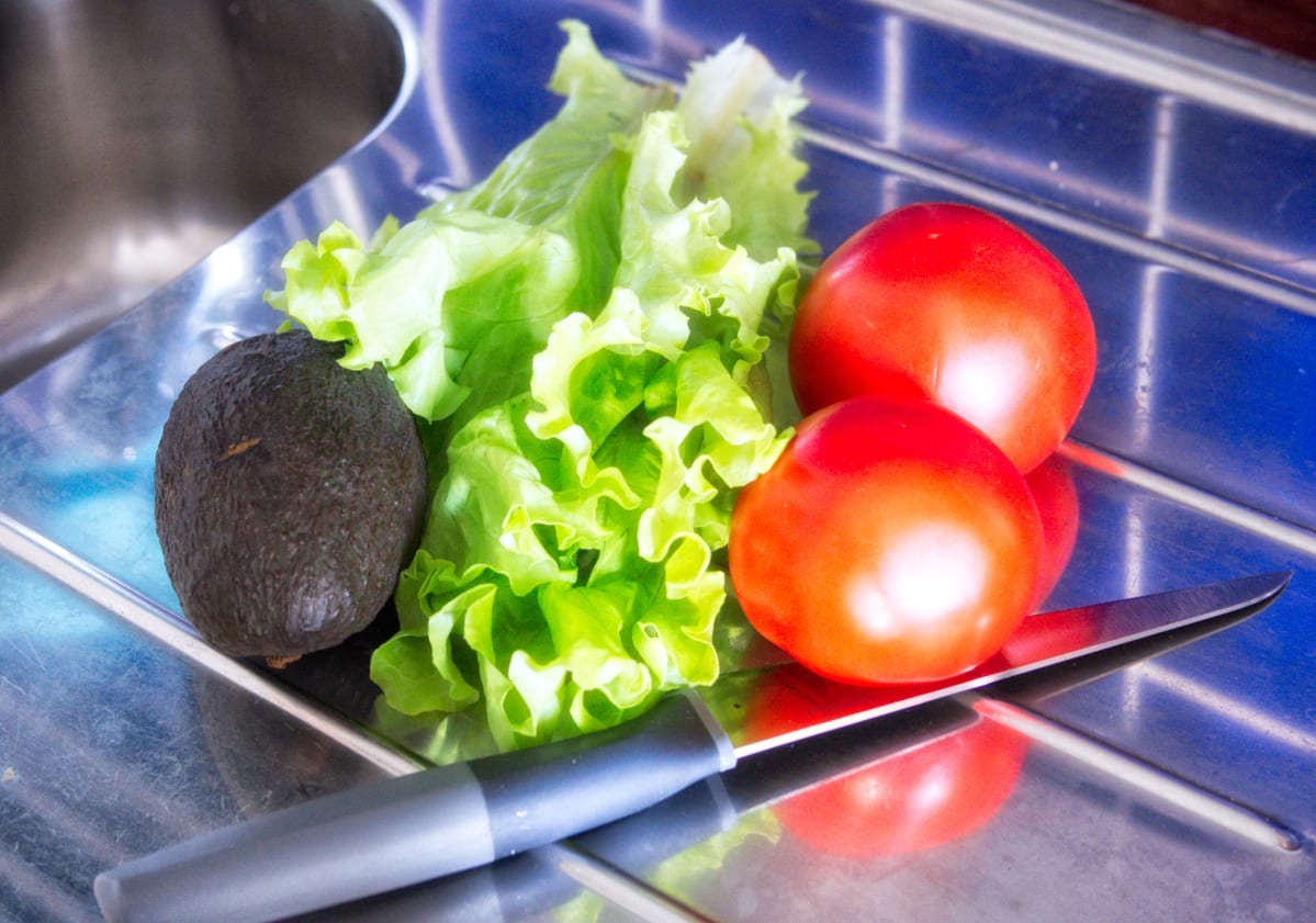 Avokado, salaaattia ja tomaatteja tiskipöydällä.