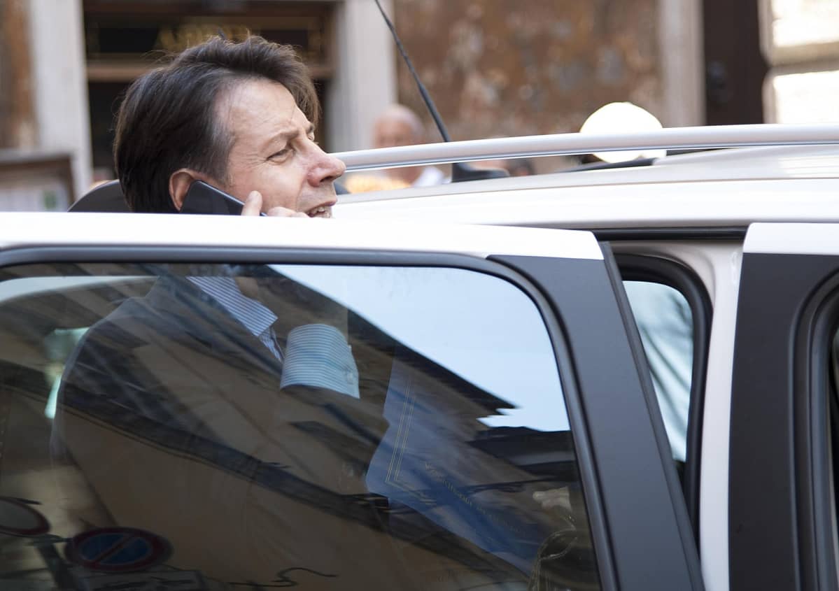 Kuvassa Giuseppe Conte on auton auki olevan oven takana puhumassa kännykkään.