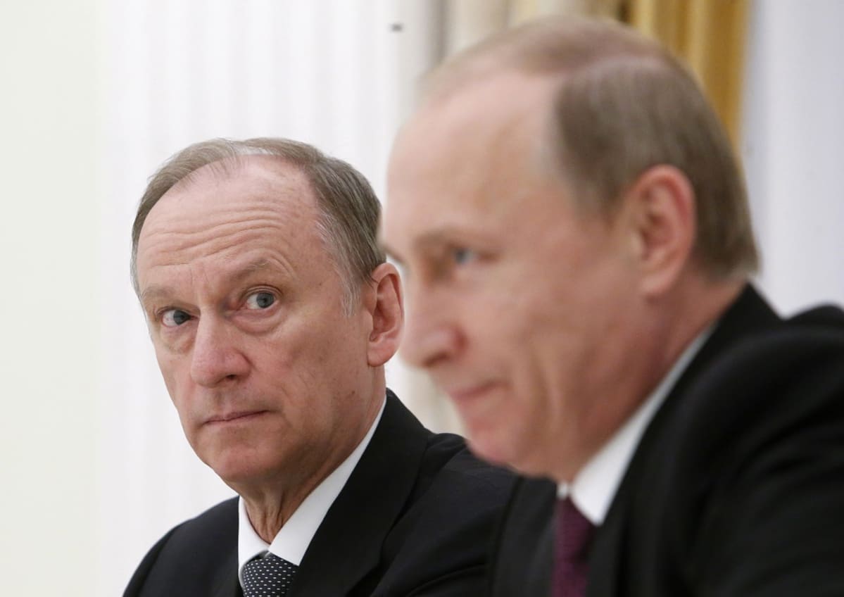 Nikolai Patrushev katsoo Putinia, joka on kuvan etualalla. Kuva on tarkennettu Patrushevin kasvoihin, Putin on kuvassa häimeä.