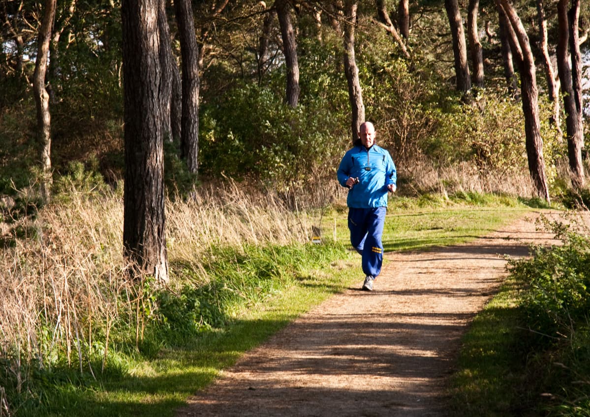 Man joggar längs med en sandväg i skogen.