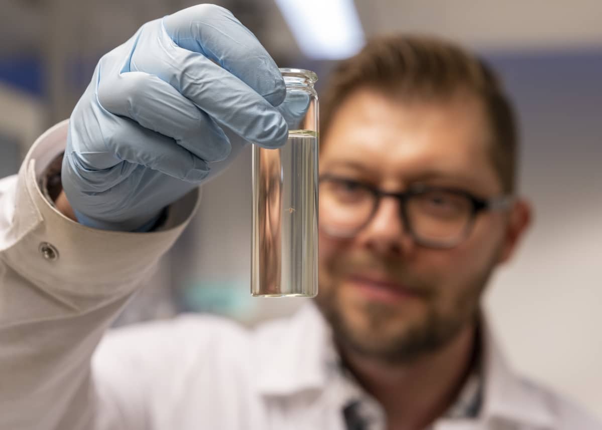 Tutkija Sami Taipale pitelee laboratoriossa käsissään pientä lasipulloa, jossa uiskentelee tutkimuksessa käytetty vesikirppu.