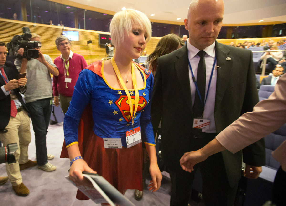 Turvamies saatteli Superwoman-asuun pukeutuneen Madeleina Kayn ulos lehdistötilaisuudesta. Kay vastustaa Britannian eroa EU:sta.