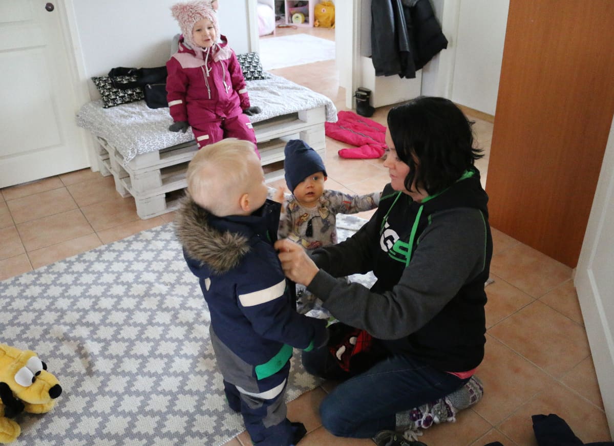 äiti pukee lapsia kotona eteisen lattialla