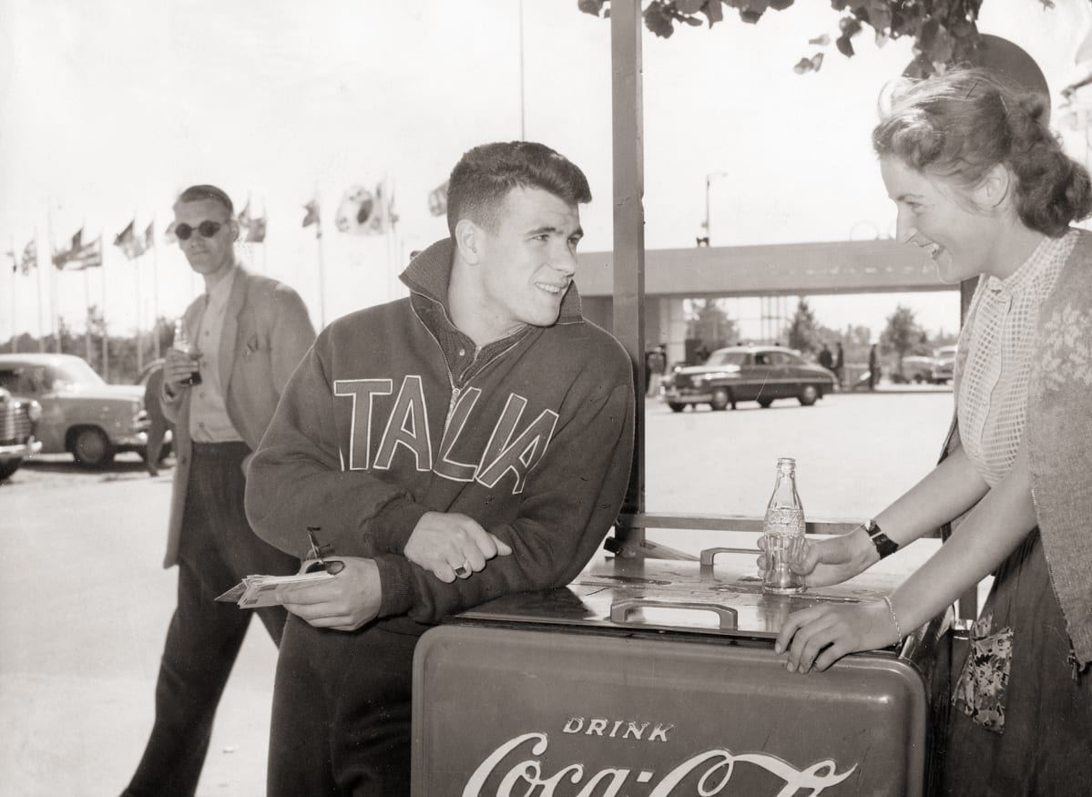 Italian joukkueen urheilija ostaa Coca-colaa myyjättäreltä.