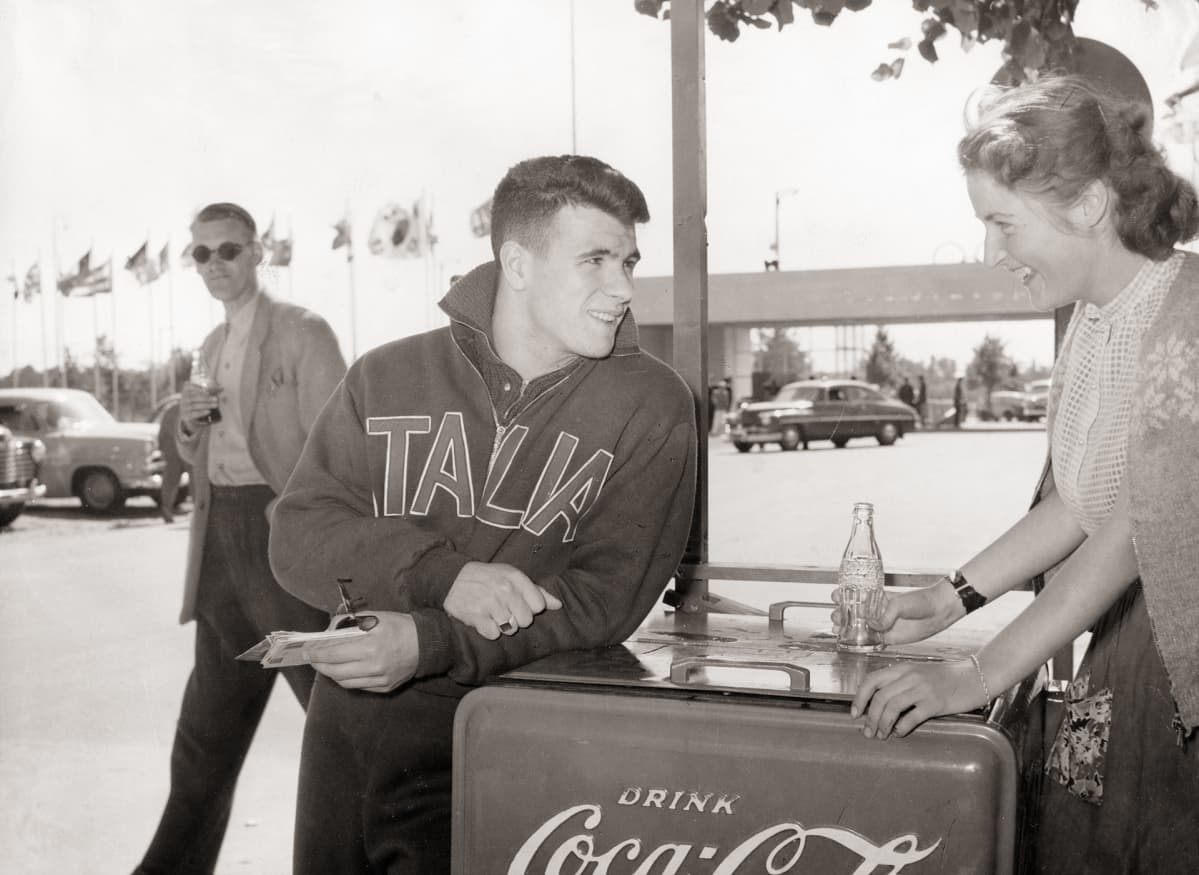 Italian joukkueen urheilija ostaa Coca-colaa myyjättäreltä.