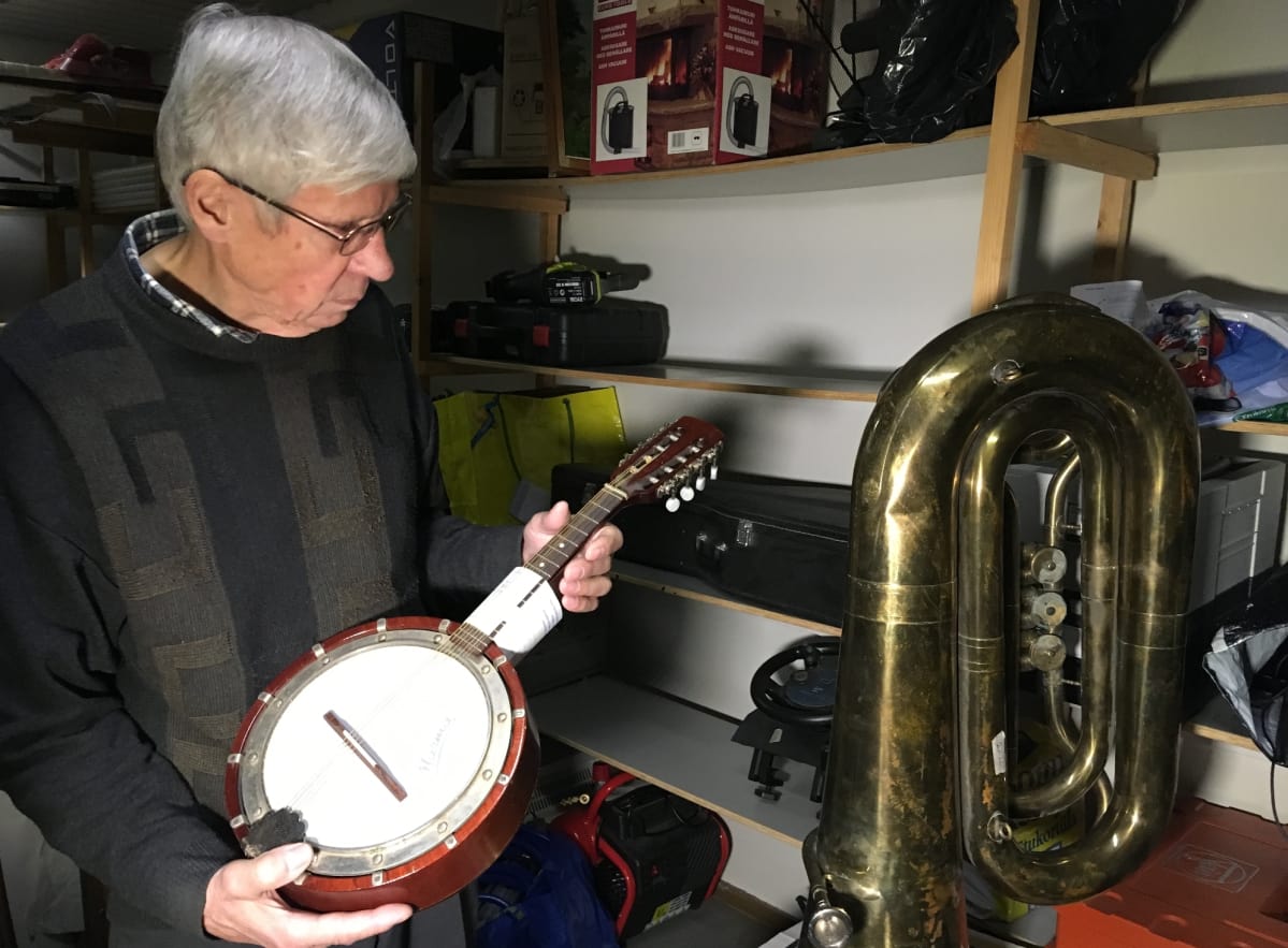 Kymen Panttilainaamon yrittäjä Seppo Heikkilä esittelee banjoa, tuuba vierellään.