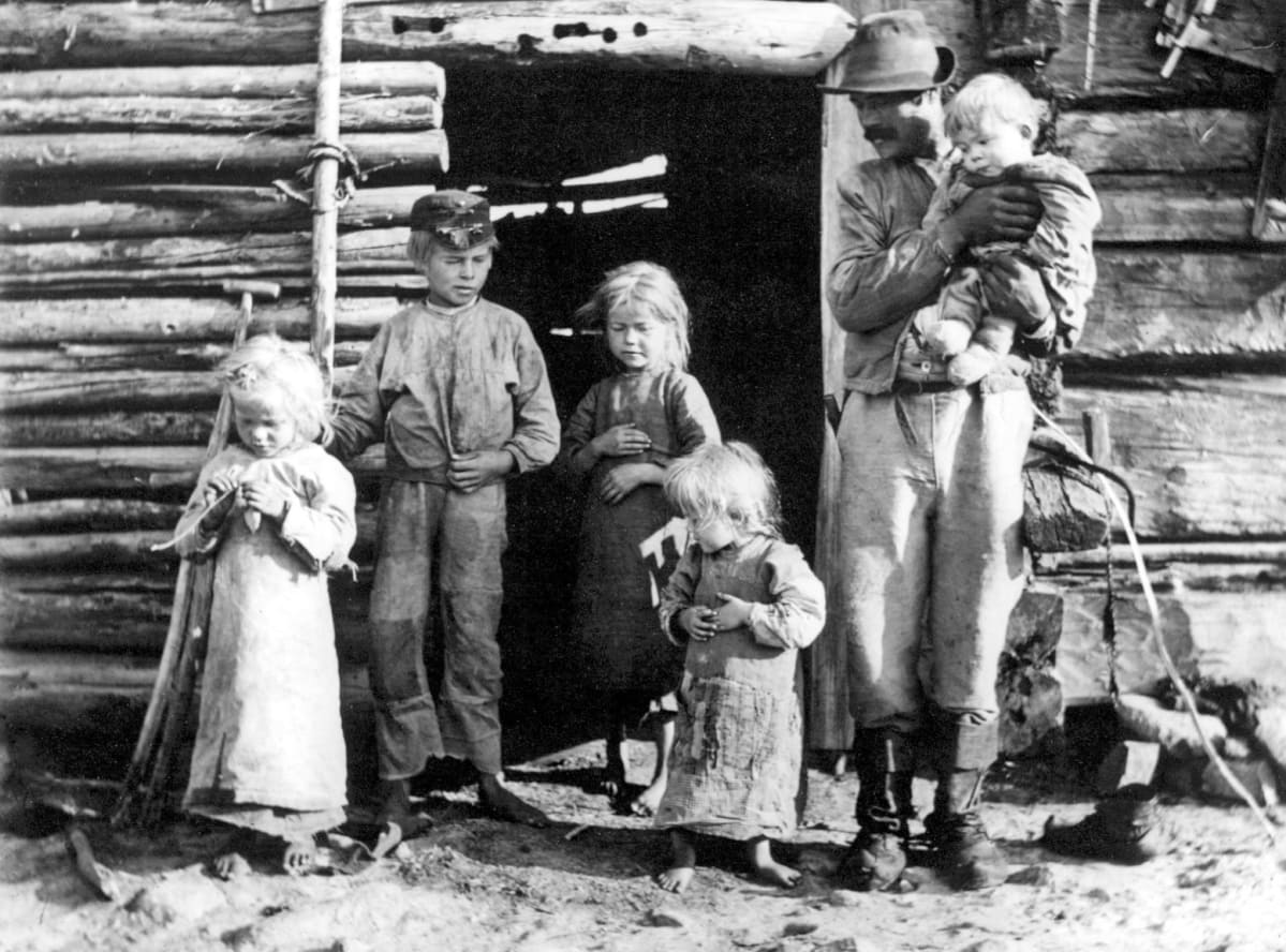 Luukkosen pettua syövä perhe hirsitalon ovella.