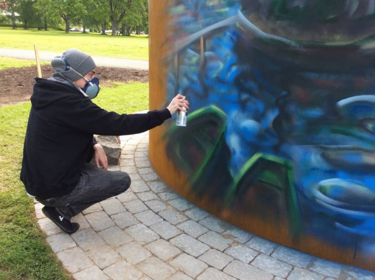 Marko Anttila maalaa graffititaidetta teräslieriön seinämään.