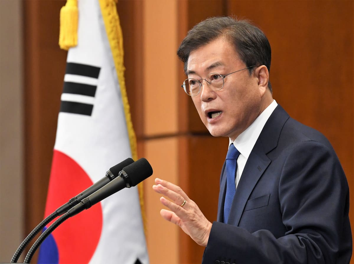 Etelä-Korean presidentti Moon Jae-in puhuu mikrofoneihin. Hänellä on silmälasit, tumma puku ja sininen kravatti. Taustalla näkyy maan lippu.