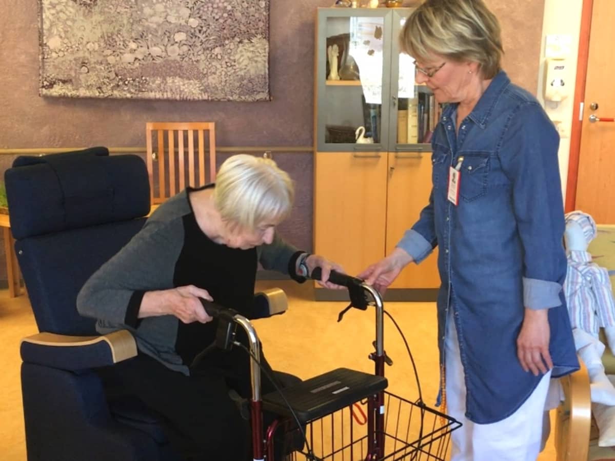 Osastonhoitaja Sirkka-Liisa Vepsäläinen auttaa naishenkilöä harjoittelemaan nousemista uudesta Armi-tuolista