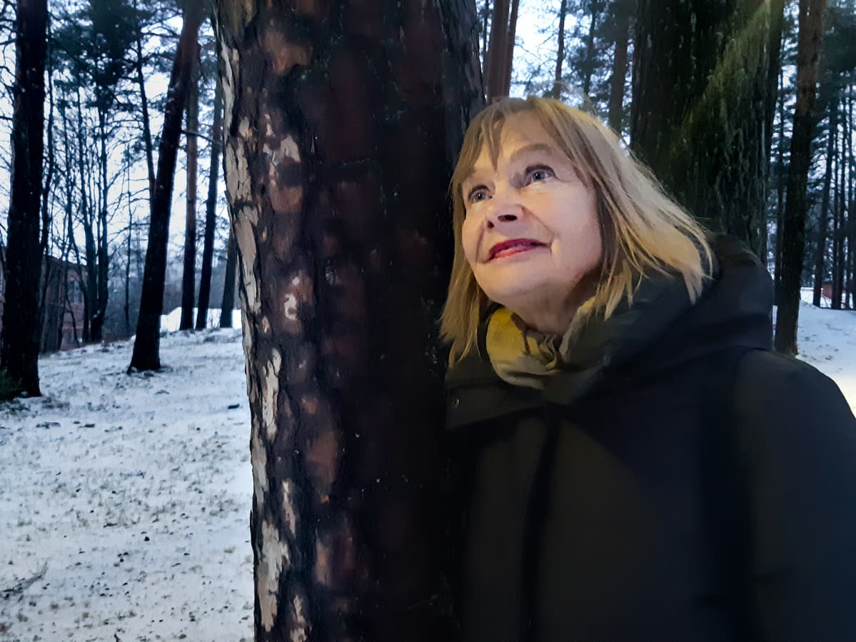 Nainen nojaa puuhun ja hymyilee.