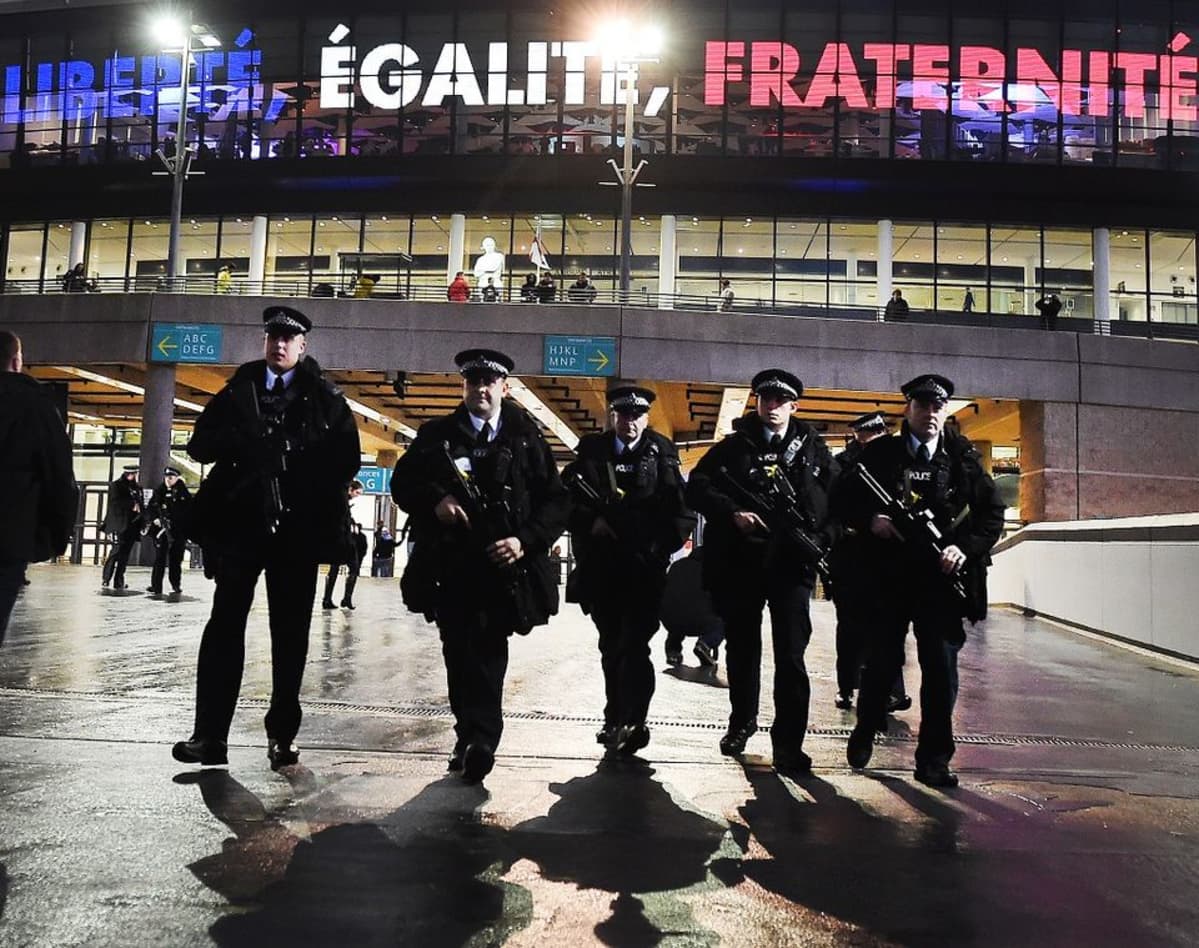 Joukko aseistettuja poliiseja. Stadionin seinälle on heijastettu ranskaksi sanat "vapaus", "tasa-arvo", "veljeys".