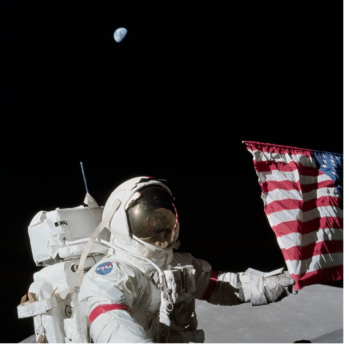 Astronautti pitelee kiinni lipun kulmasta. Taustalla avaruudessa häämöttää maapallo.