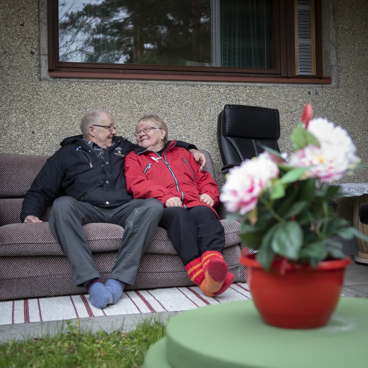 Ikääntynyt pariskunta lähekkäin sohvalla. Molemmat hymyilevät.